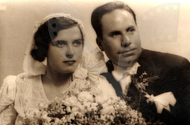 Ein Schwarz-Weiß-Foto eines lachenden Mannes und einer Frau an ihrem Hochzeitstag, die Frau in einem weißen Kleid mit einem Strauß Blumen in der Hand und der Mann neben ihr.