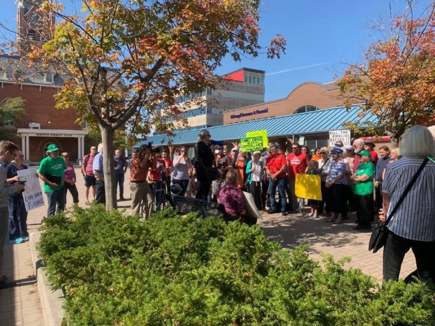 Eine Gruppe von Menschen demonstriert vor einem Gebäude auf dem Campus der University of Michigan, hält Schilder und trägt einige Kameras und Taschen bei sich.