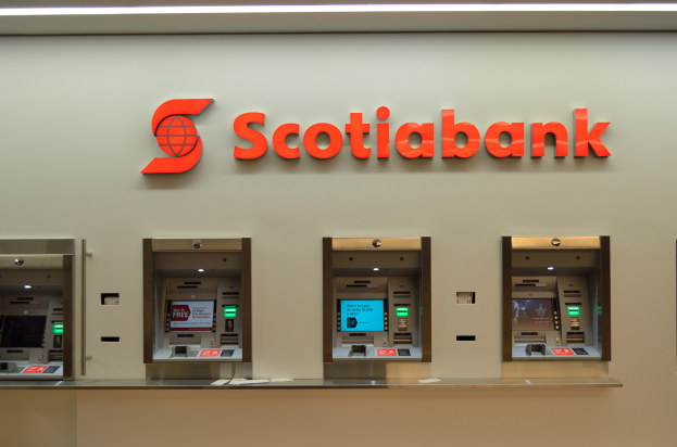 Ein modernes Scotiabank-Geldautomatengerät mit schwarzer und silberner Optik, einem großen Display und Bedientasten, vor einem hellgrauen Hintergrund mit gerahmten Bildern und der Aufschrift "Scottish Bank"