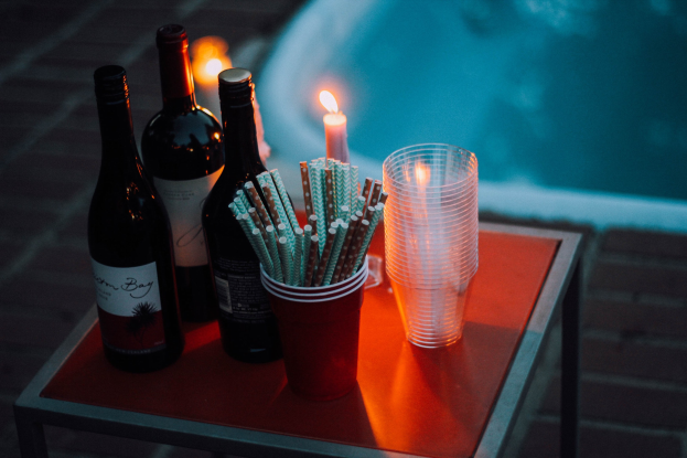 Ein Tisch am Swimmingpool mit zwei Weinflaschen, einer Kerze, Gläsern und Strohhalmen deutet auf einen Abend am Pool hin.