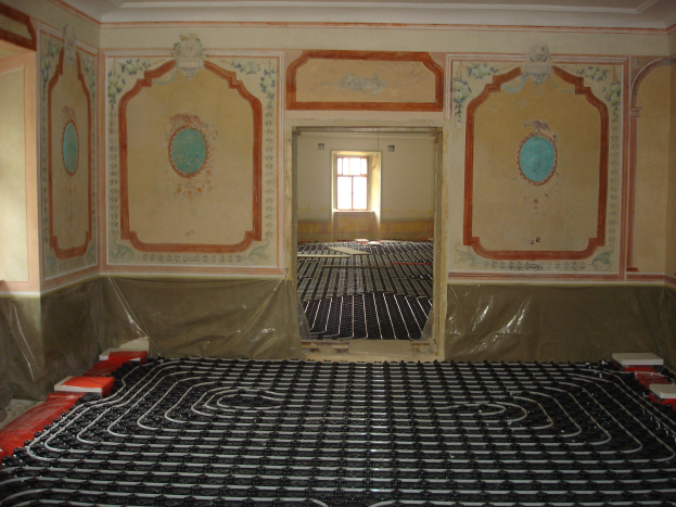 Ein Raum mit einer Fußbodenheizung in der Mitte, umgeben von Wänden und einem Fenster, mit verschiedenen Gegenständen auf dem Boden in der Nähe des Systems.