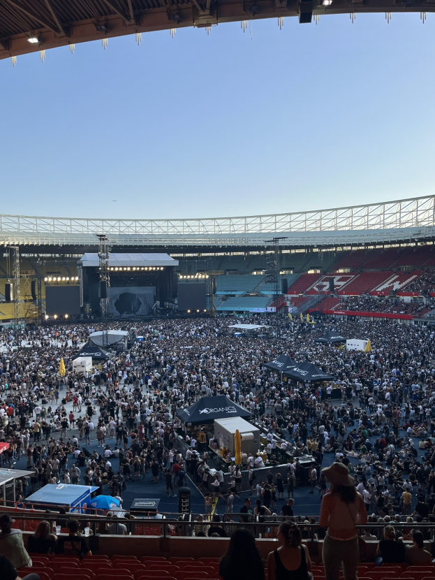Große Menschenmenge auf Tribünen und im Stehen in einem Stadion mit Zelten, Geländern und Scheinwerfern am Himmel
