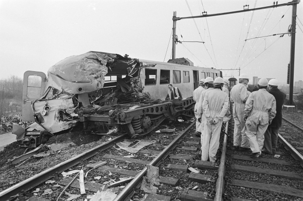 Schwarz-weiß-Bild einer Zugkollision auf den Gleisen mit Einsatzkräften in Helmen und einem Hintergrund von Strommasten, Bäumen, Gebäuden und einem klaren Himmel.