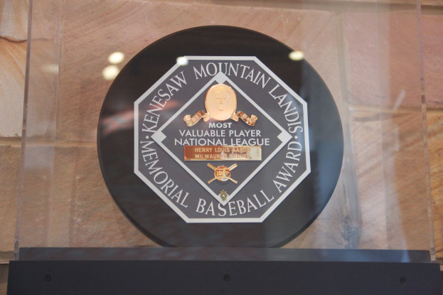 Schwarze Plakette an einer Gebäudewand mit der eingravierten Inschrift "Mountain Lands Memorial Baseball Award" und einem Hintergrund.