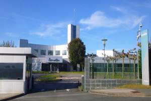 Ein großes Gebäude mit zahlreichen Fenstern und einem Tor davor, umgeben von Straßenlaternen, Gittern, Bäumen, Gras und einem bewölkten Himmel, das als Hauptsitz von Iberostica in den Niederlanden dient.
