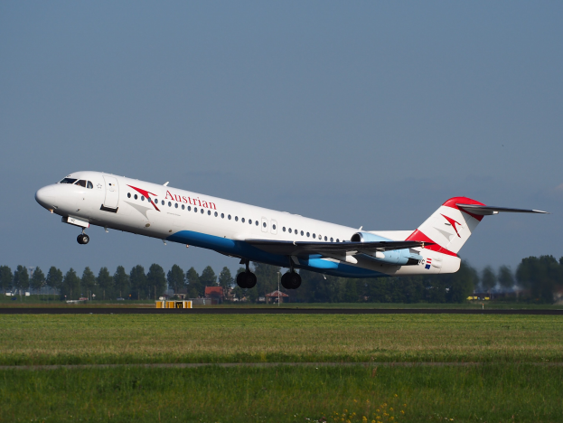 Ein Embraer ERJ-190-Flugzeug der Austrian Airlines startet vom Frankfurter Flughafen, mit grünem Gras, Bäumen, Gebäuden und Himmel im Hintergrund.