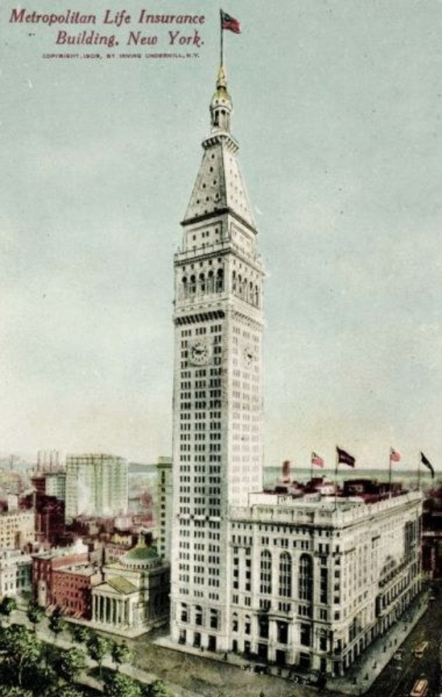 Schwarz-weiß-Postkarte des Metropolitan Life Insurance Building in New York City, das eine belebte Stadtkulisse mit mehreren Gebäuden, Bäumen und Fahrzeugen auf der Straße zeigt.