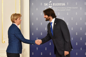Bundeskanzlerin Angela Merkel und Bundeskanzler Joachim Gauck schütteln sich die Hände vor einer Wand mit einem 'EU-Gipfel'-Banner und einer Tür im Hintergrund, beide lächeln.