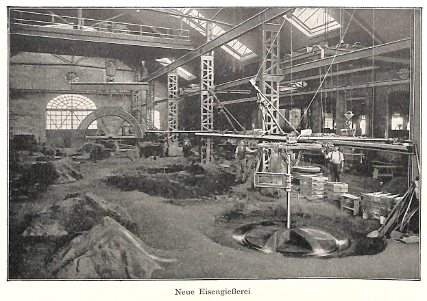 Schwarz-weiß-Fotografie eines Fabrikinneren mit Arbeitern an Maschinen, Metallstangen und -rohren, beschriftet mit "Neue Eisengießerei, die erste Fabrik Deutschlands" unten.