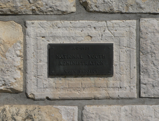 Steinwand mit einem rechteckigen Schild, auf dem "Nationales Jugendamt" in weißer, fetter Schrift auf einem schwarzen Hintergrund steht.