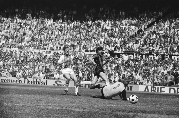 Schwarz-weiß-Foto von Männern, die auf einem Feld Fußball spielen, mit Zuschauern im Hintergrund und einem Banner mit der Aufschrift "Bundesliga 1978-79 Ajax 1-1 Hannover 96."
