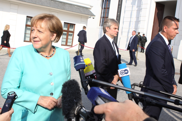 Bundeskanzlerin Angela Merkel spricht mit Reportern vor dem Bundeskanzleramt in Berlin, umgeben von Menschen mit Mikrofonen und Gebäuden im Hintergrund.
