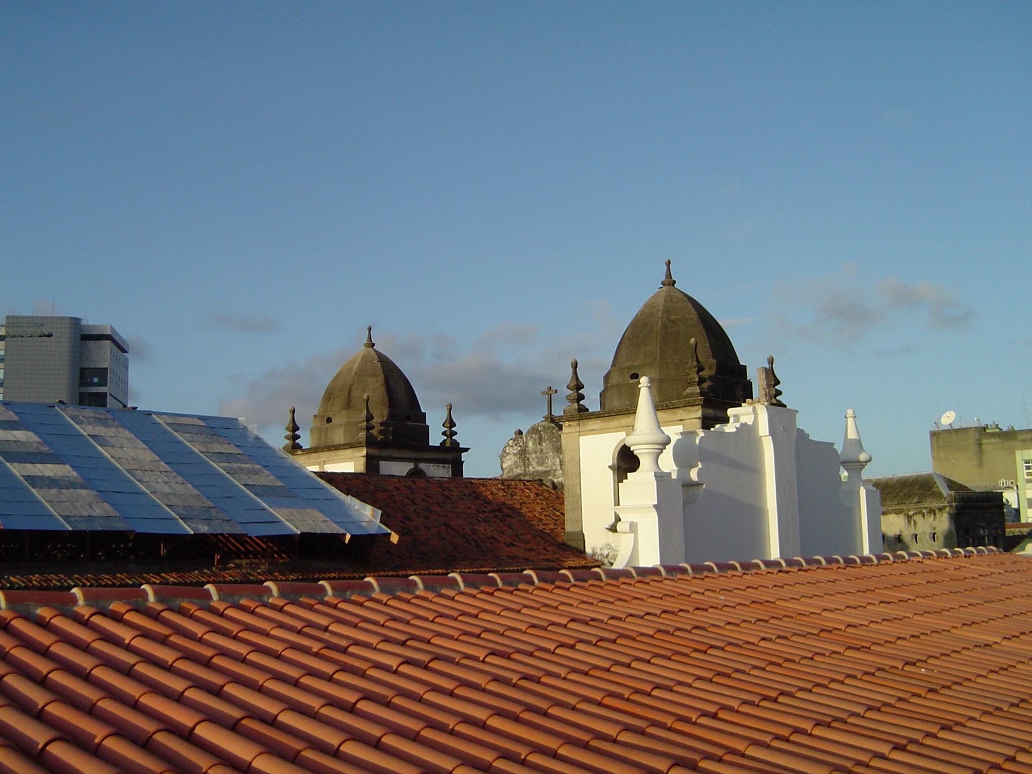 Stadtansicht mit Gebäuden im Vordergrund, einem blauen Himmel im Hintergrund und Solarpanelen auf einem Dach, die den Einsatz erneuerbarer Energien anzeigen.
