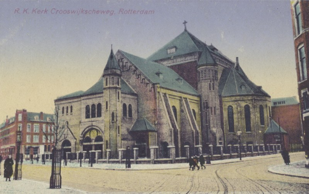 Altes Foto einer Kirche in städtischer Umgebung mit umgebenen Gebäuden, Straßeninfrastruktur, Fahrzeugen, Fußgängern, Bäumen und einem klaren Himmel mit Text oben.