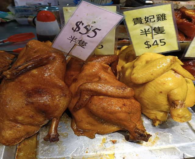 Hühner auf einem Metalltablett mit Preisschildern in einem Marktumfeld mit verschiedenen Gegenständen im Hintergrund.