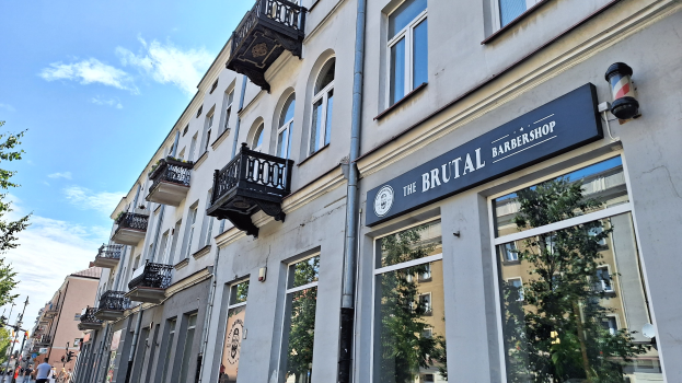 Brutalistische Barbershop-Fassaden in Berlin mit Betongebäuden, Fenstern, Geländern, Balkonen, Schildern, Bäumen, Straßenlaternen, Passanten und einer bewölkten Himmel.
