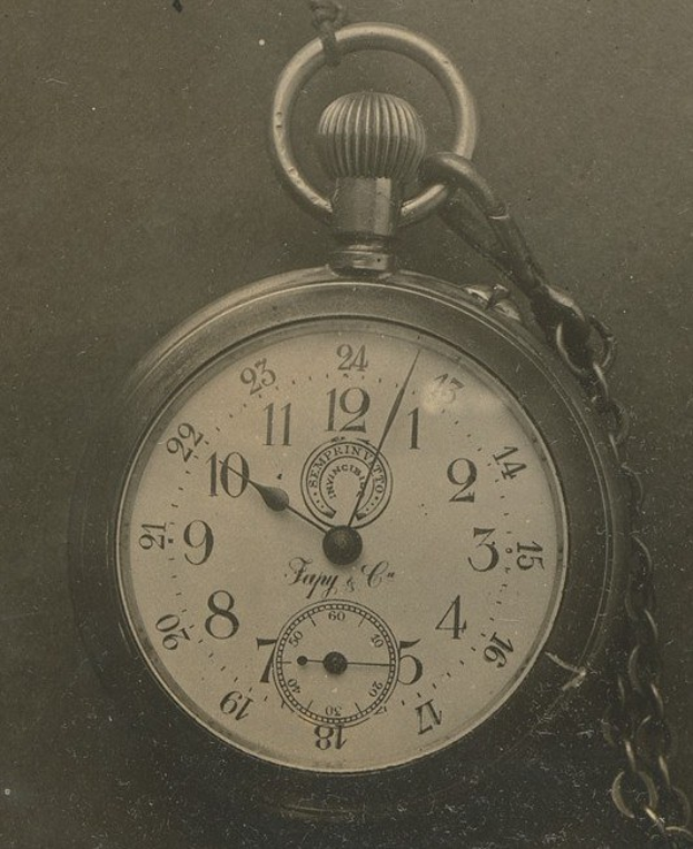Ein Schwarz-Weiß-Foto einer antiken Taschenuhr mit einer Kette, das eine nummerierte Uhr zeigt.