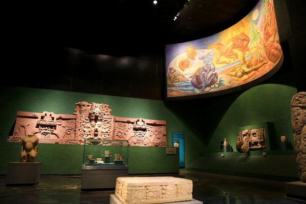 Ausstellung verschiedener Artefakte im Anthropologischen Museum von Mexiko-Stadt, darunter Skulpturen, Tischgegenstände, eine Texttafel, eine Wandmalerei und Deckenbeleuchtung.