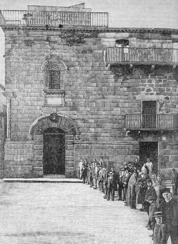 Schwarzes und weißes Foto einer Gruppe jüdischer Gefangener, die vor dem Eingang einer Synagoge in Jerusalem stehen, mit einem Gebäude mit Fenstern, Geländern und einer Tür dahinter.