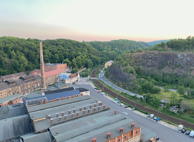 Luftaufnahme einer Stadt mit dichtem Gebäudebestand, Straßen voller Fahrzeuge, Strommasten, vereinzelten Bäumen, fernen Hügeln und einem bewölkten Himmel, die an ein Kohlerevier erinnern.