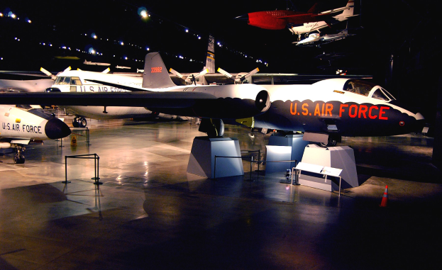 Eine Gruppe von Kampfflugzeugen in einem schwach beleuchteten Museum ausgestellt, umgeben von St├Ąnden, Verkehrskegeln und anderen Gegenst├Ąnden auf dem Boden.