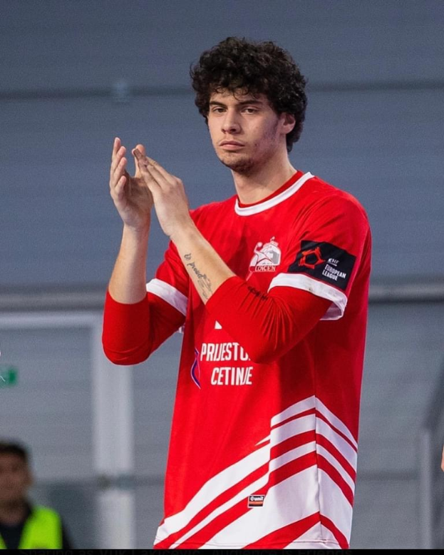 Ein Mann in einem roten und weißen Hemd klatscht in der Vordergrund mit einer anderen Person und einer Wand im Hintergrund, mit dem Text "Copenhagen Futsal Club - Foto 1" unten.