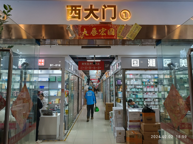 Innenseite einer chinesischen Apotheke mit Glaswänden, Regalen, verstreuten Kartons, einer Pflanze auf der linken Seite und einem Namensschild oben.