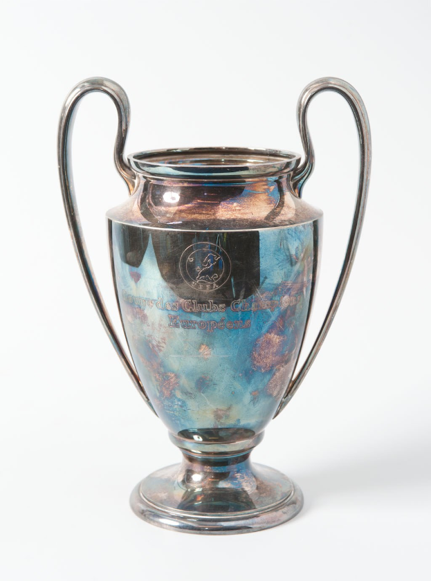 Der UEFA-Champions-League-Pokal, ein stahlerner Becher mit zwei Handles und einem blauen und silbernen Farbschema, beschriftet mit «UEFA Champions League», gegen einen weißen Hintergrund dargestellt.