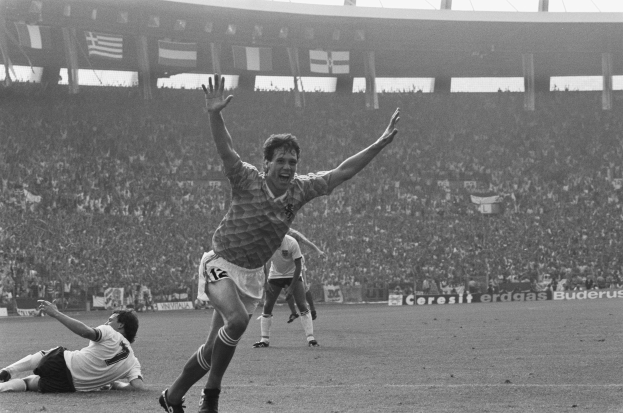 Schwarzes und weißes Foto eines Fußballspielers, der ein Tor mit Teamkollegen und Fans in einem Stadion feiert.