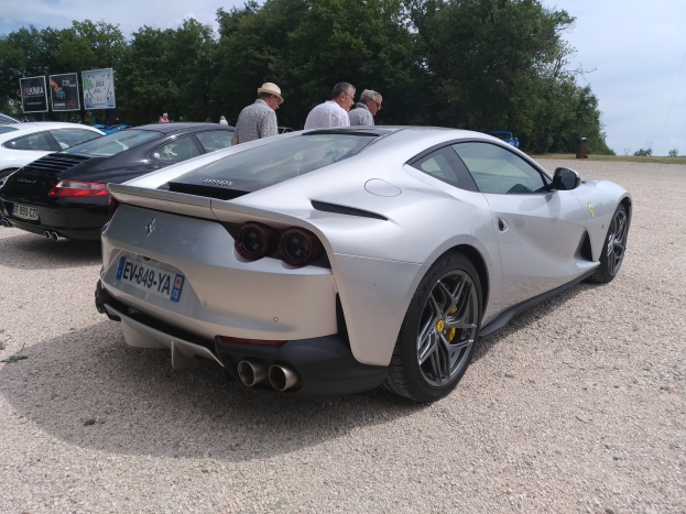 Roter Ferrari 812 Superfast beim Goodwood Festival of Speed, umgeben von Menschen mit Mützen, Bäumen, Schildern und einem bewölkten Himmel.