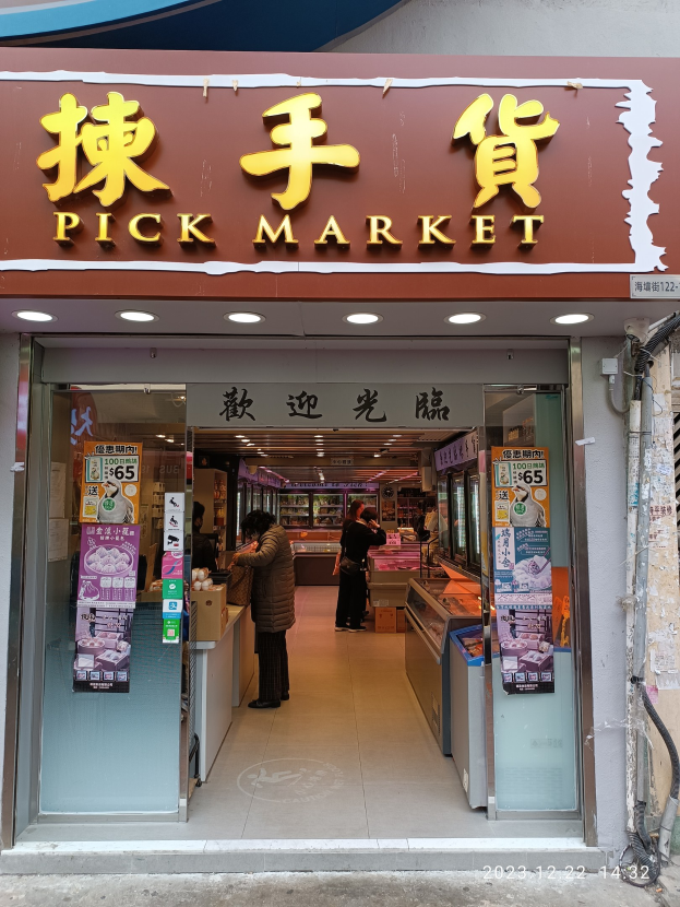 Ein belebter Hongkonger Straßenmarkt mit ein paar Menschen, die an Ständen stöbern, mit einer Wand mit freiliegenden Rohren auf der rechten Seite.