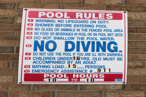 Weißer Schild mit schwarzer Schrift, auf dem "Pool Rules: No Diving" steht, an der Seite eines Backsteingebäudes angebracht.