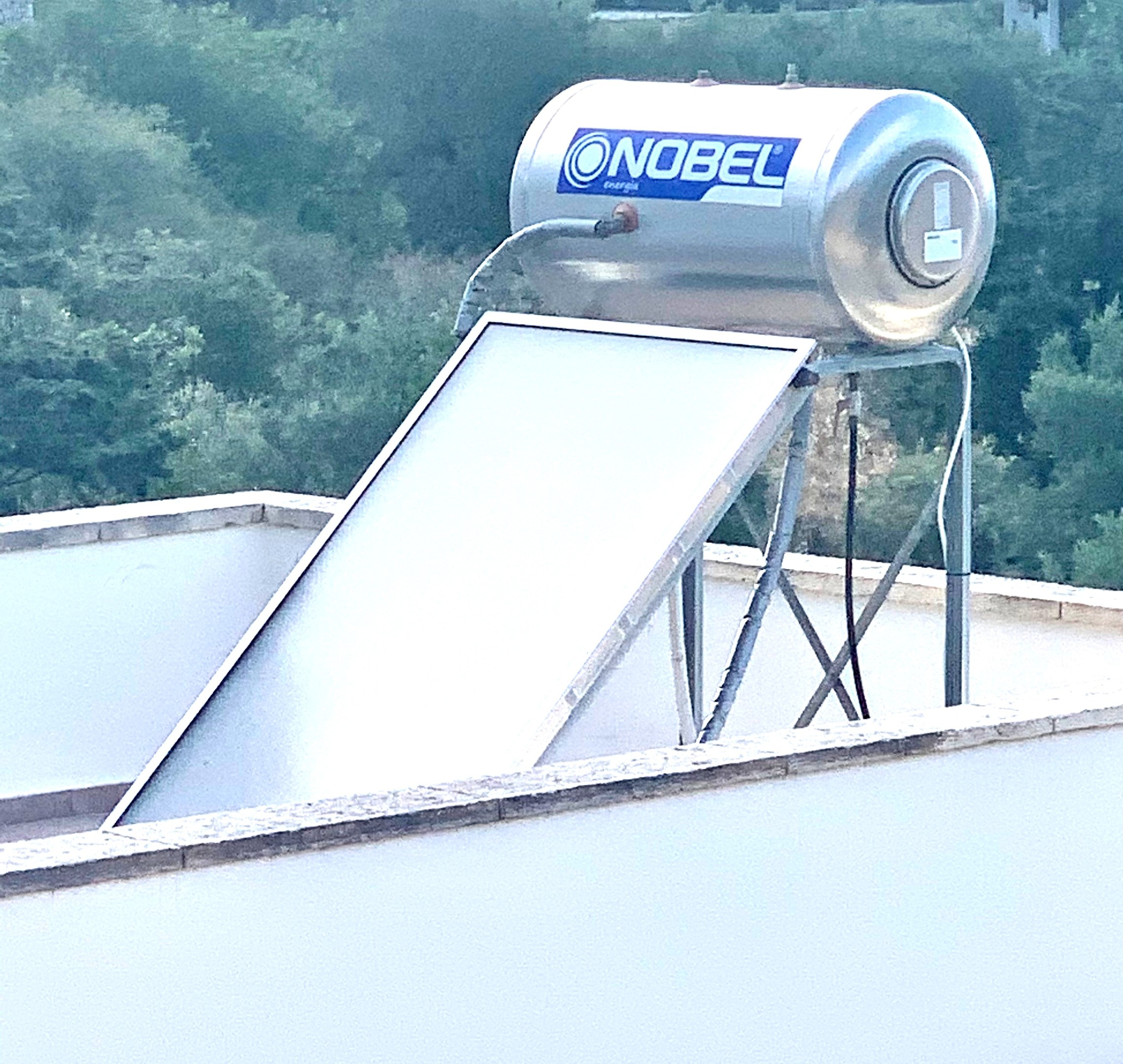 Solarwassererhitzer mit Speicher auf einem Gebäude auf dem Dach montiert, Bäume im Hintergrund sichtbar.