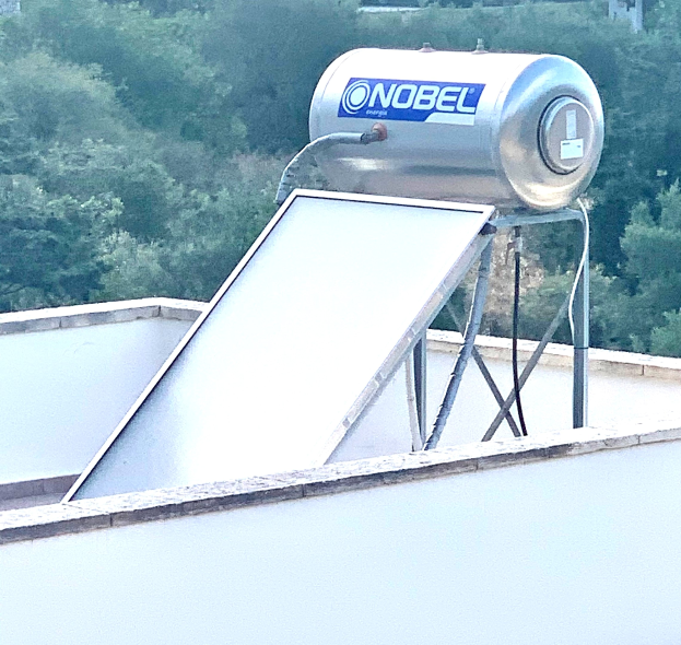 Solarwassererhitzer mit Speicher auf einem Gebäude auf dem Dach montiert, Bäume im Hintergrund sichtbar.