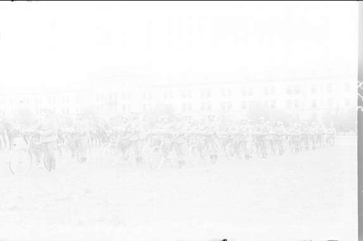 Schwarzes und weißes Foto von Radfahrern, die im Schnee an einem Gebäude vorbeifahren.