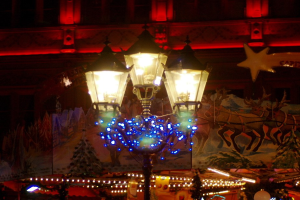 Eine mit Lichtern und Dekoration geschmückte Straßenlaterne steht nachts in einer Stadt, im Hintergrund ist ein Gebäude zu sehen.
