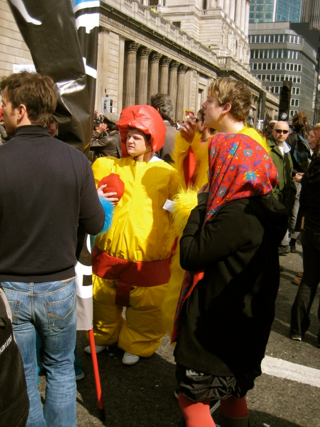 Ein Clown steht in der Mitte des Bildes, mit Menschen auf der linken und rechten Seite und Geb├Ąuden ├╝berkopf.
