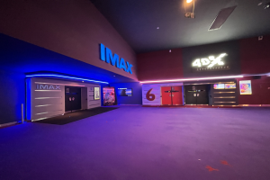 Innenseite eines Kinos mit lila Teppichboden, Text und Bildschirmen an den Wänden und Deckenbeleuchtung.