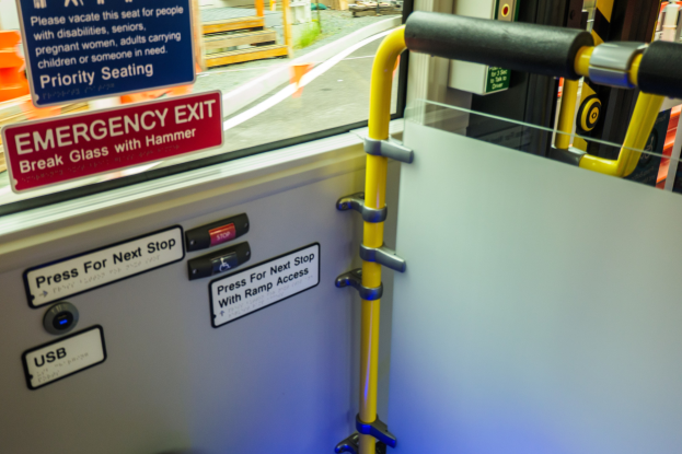 Notausgangsschild an der Seite eines Zuges mit einer Tür, Griff und Glasfenster, das die Straße und Pfosten draußen zeigt.