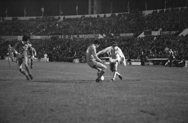 Schwarzes und weißes Bild von Männern, die Fußball in einem Stadion mit Zuschauern in den Rängen und Fahnen im Hintergrund spielen.
