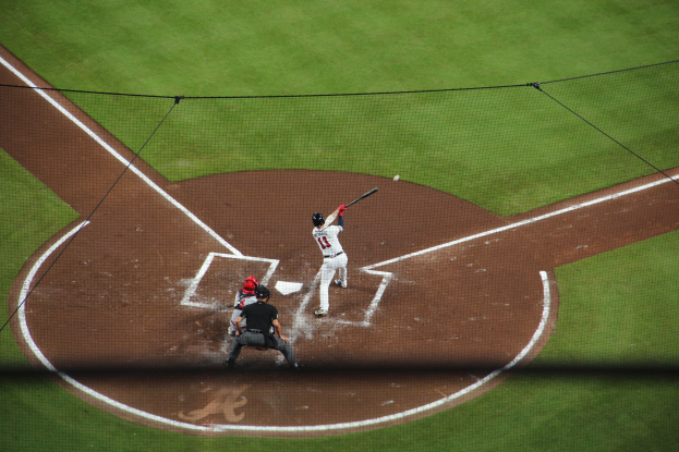 Ein Baseballspieler in einem Sportoutfit schwingt einen Schläger auf einem grünen Feld, mit einem Netz im Hintergrund.