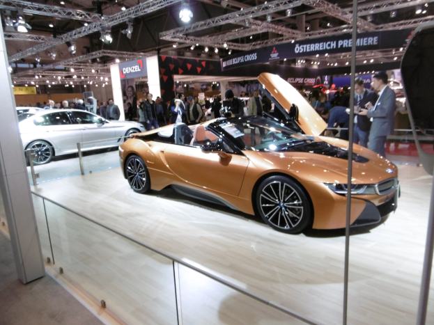 Ein stylischer schwarzer BMW i8 Roadster mit Chromakzenten auf der Frankfurt Motor Show umgeben von elegant gekleideten Gästen in einer Atmosphäre der Aufregung.