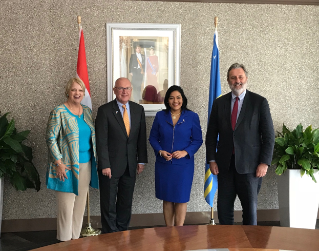 Eine Gruppe strahlender Menschen um einen Tisch mit Papieren herumstehend, umgeben von Fahnen, Topfpflanzen und einem Foto auf der Wand, feiert die Unterzeichnung eines Memorandums von Verständnis zwischen den Vereinigten Staaten und Kanada.