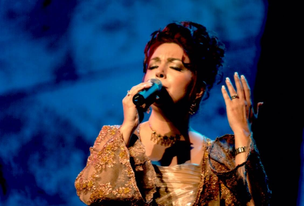 Eine Frau in einem goldenen Kleid singt auf der Bühne der Eurovision Song Contest mit einem blauen und schwarzen Hintergrund.