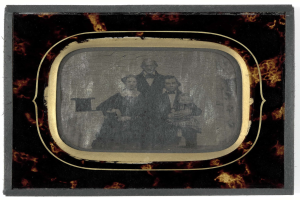 Schwarz-weiß-Foto eines Mannes im Anzug und Schlips und einer Frau in unbekannter Kleidung vor einem alten Fernseher, beide mit ernsten Gesichtern.