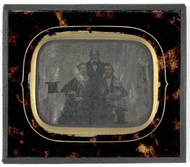 Schwarz-weiß-Foto eines Mannes im Anzug und Schlips und einer Frau in unbekannter Kleidung vor einem alten Fernseher, beide mit ernsten Gesichtern.