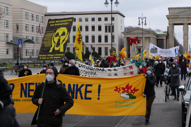 Große Gruppe von Menschen bei einer Straßendemonstration gegen Atomkraft in Deutschland, mit Schildern und Fahnen, begleitet von Fahrzeugen und Gebäuden im Hintergrund.