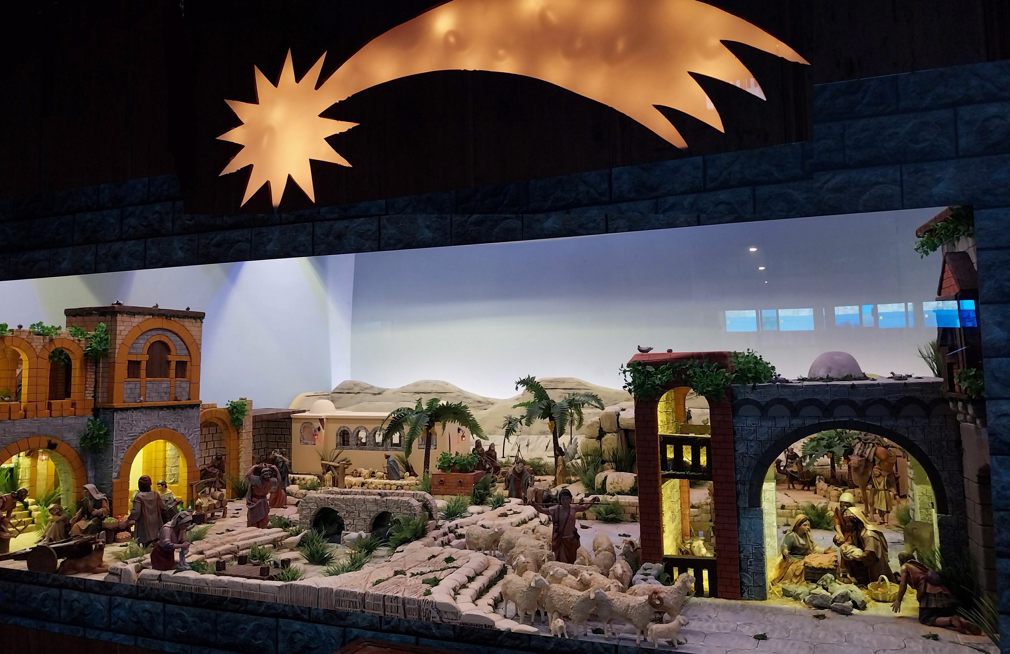 Eine Krippenausstellung im Museum mit beleuchteten Figuren, Tieren und Strukturen an einer Wand.