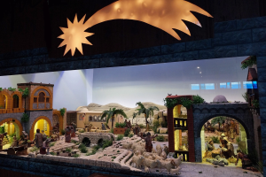 Eine Krippenausstellung im Museum mit beleuchteten Figuren, Tieren und Strukturen an einer Wand.