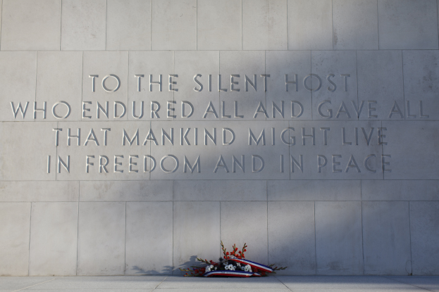 Eine Gedenkwand mit einer Inschrift, die denjenigen ehrt, die aushielten und gaben für Freiheit und Frieden, umgeben von einem Blumenstrauß.